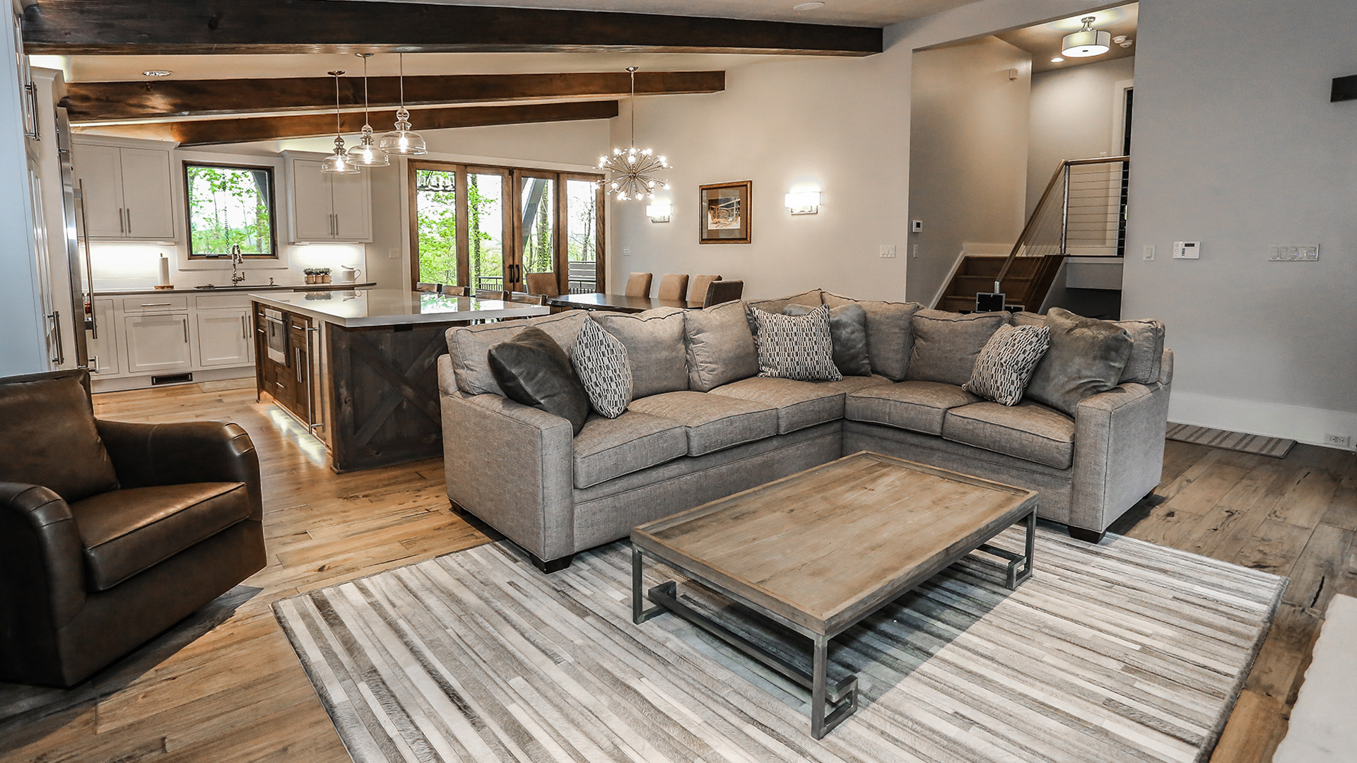 interior shot of greystone's living area. The colors in the room are a neutral gray tone. There is a plush couch surrounding a wooden coffee table. It is an open floor plan with exposed wooden beams on the ceiling.