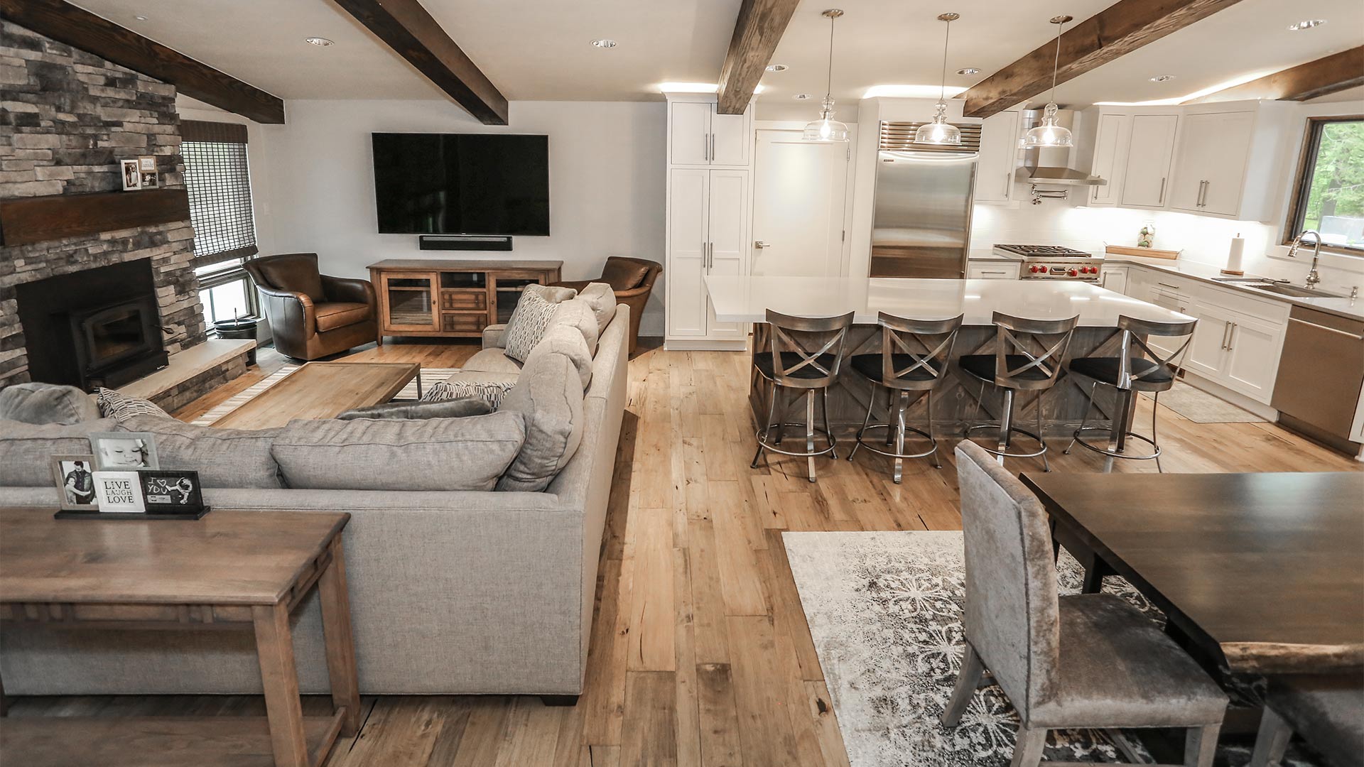 an interior shot of the open floor planning common area. There is a sitting area with a sectional couch and tv. There is a formal dining area and a kitchen with an island.