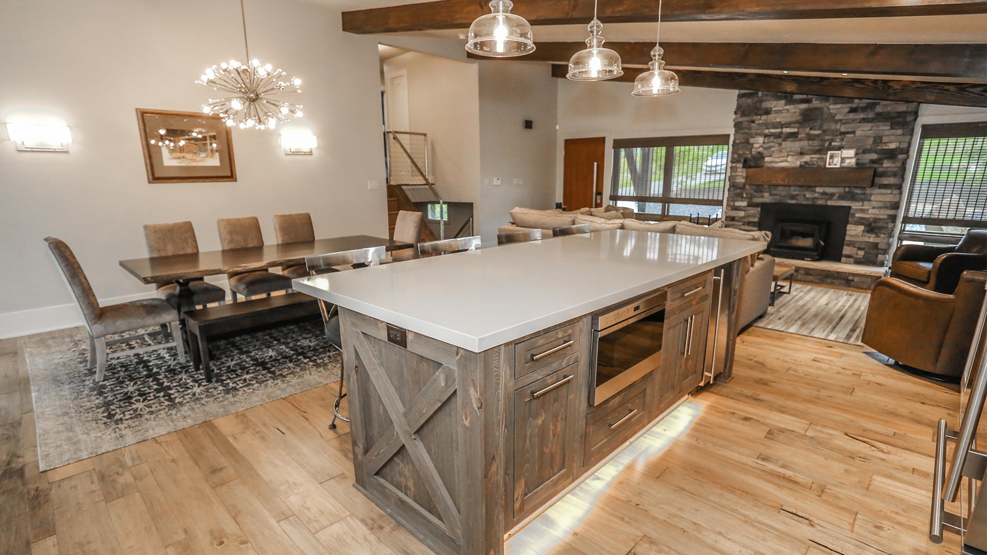 detail shot of the kitchen island. The island is styled in a country style with gray wood and sleek gray countertop. There are chairs for dining on one side of the island and appliances and storage space on the other.