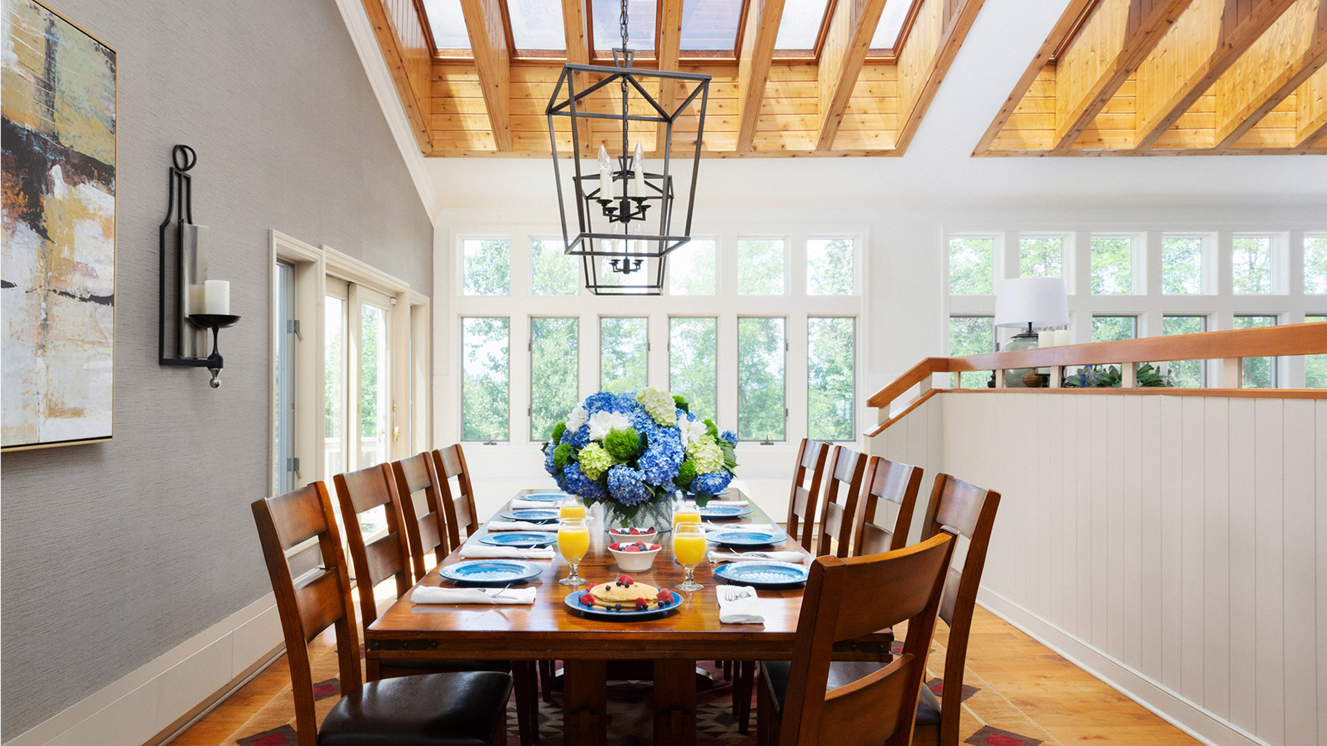 interior shot of the arden dining room. There is a long dark wood table with matching chairs. There are windows around the room and a large chandelier above the elegantly set table.