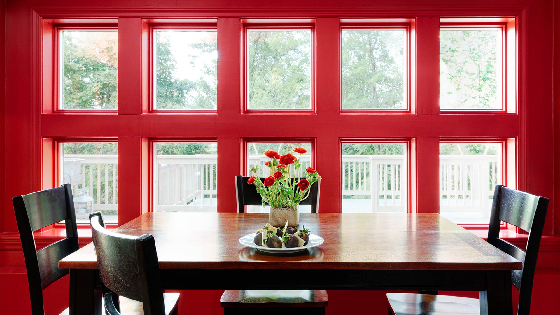 interior shot of a breakfast nook in arden. The walls are a dark red and the table is dark wood. There are flowers set in the middle of the table.