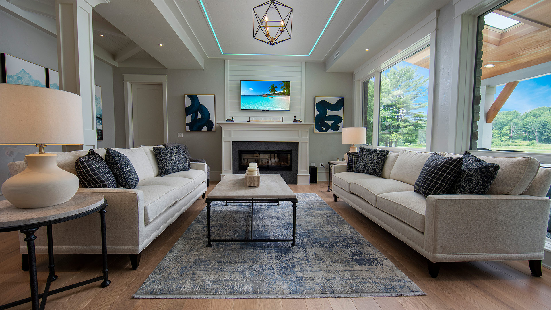 an interior shot of the living area. There are two neutral colored couches across from each other with a coffee table between them. There is a fireplace with modern art pieces on either side of the mantle.