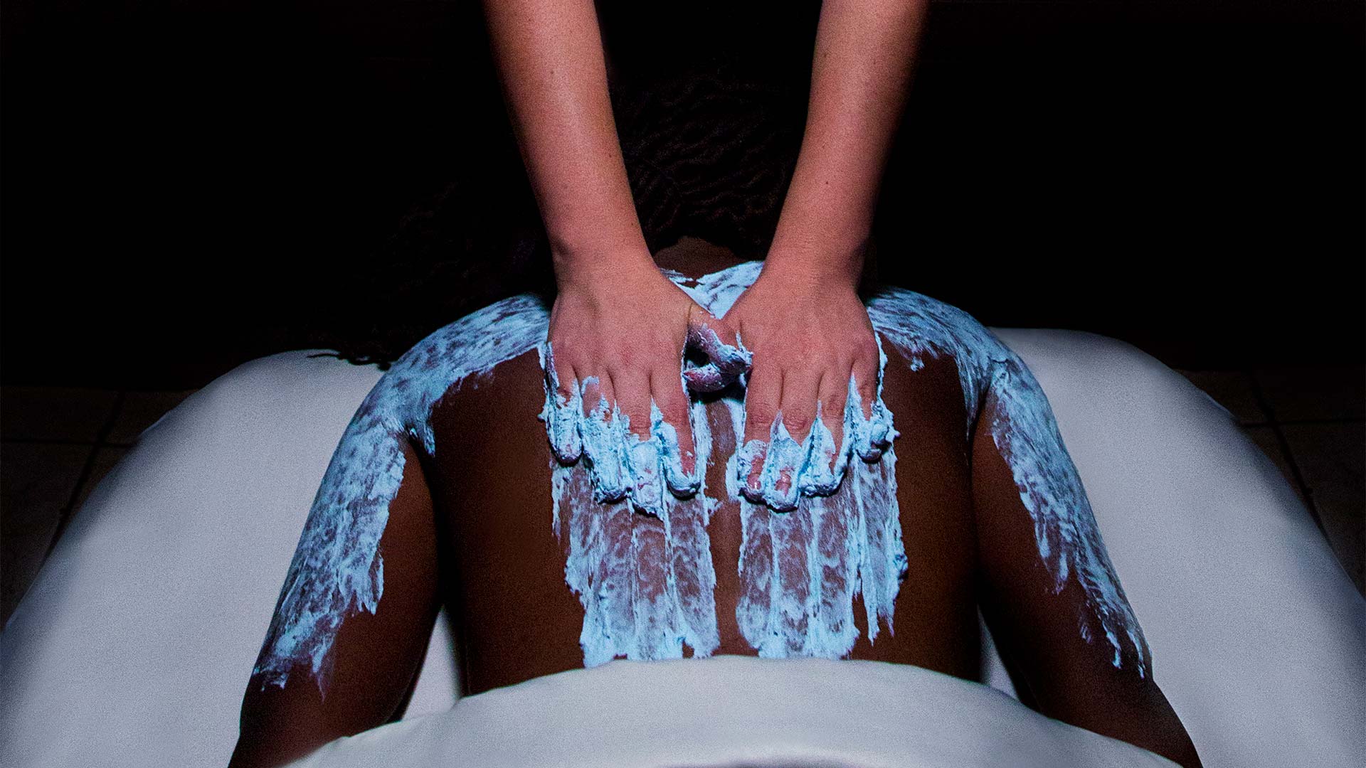 a person getting a spa treatment. They are laying face down and a are having a blue paste being applied to their back and arms.
