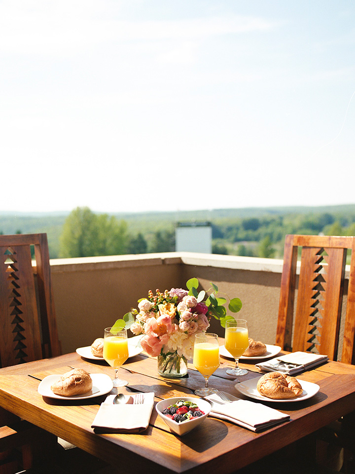 a detail shot of a table sitting on a balcony. There is an elegant brunch spread on the table and sweeping views of the resort grounds in the distance