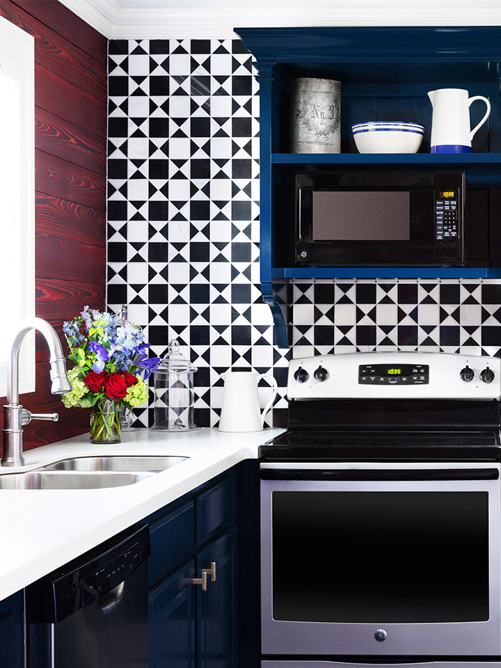 an interior shot of the full kitchen in the townhomes. The tiling is a geometric black and white print. There is a sink, a full fridge, an over and stovetop. There is ample counter and storage space.
