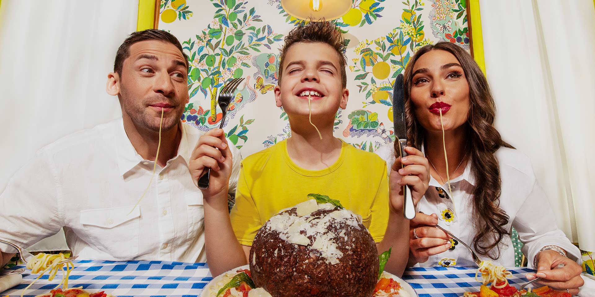 parents with their young son are slurping on spaghetti noodles and smiling