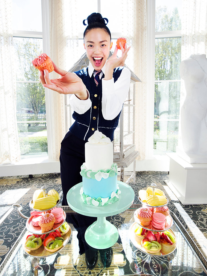 A girl in front of a table of deserts holding up two cupcakes
