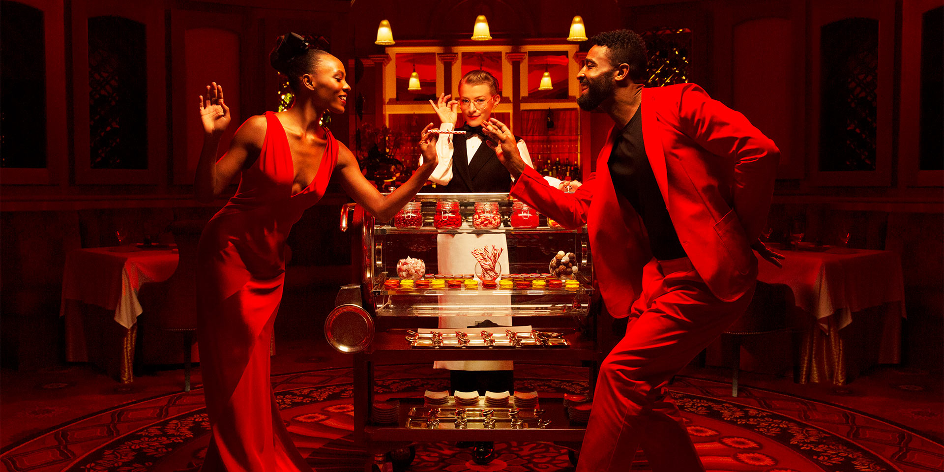 a man and woman dancing with a server with a cart standing behind them