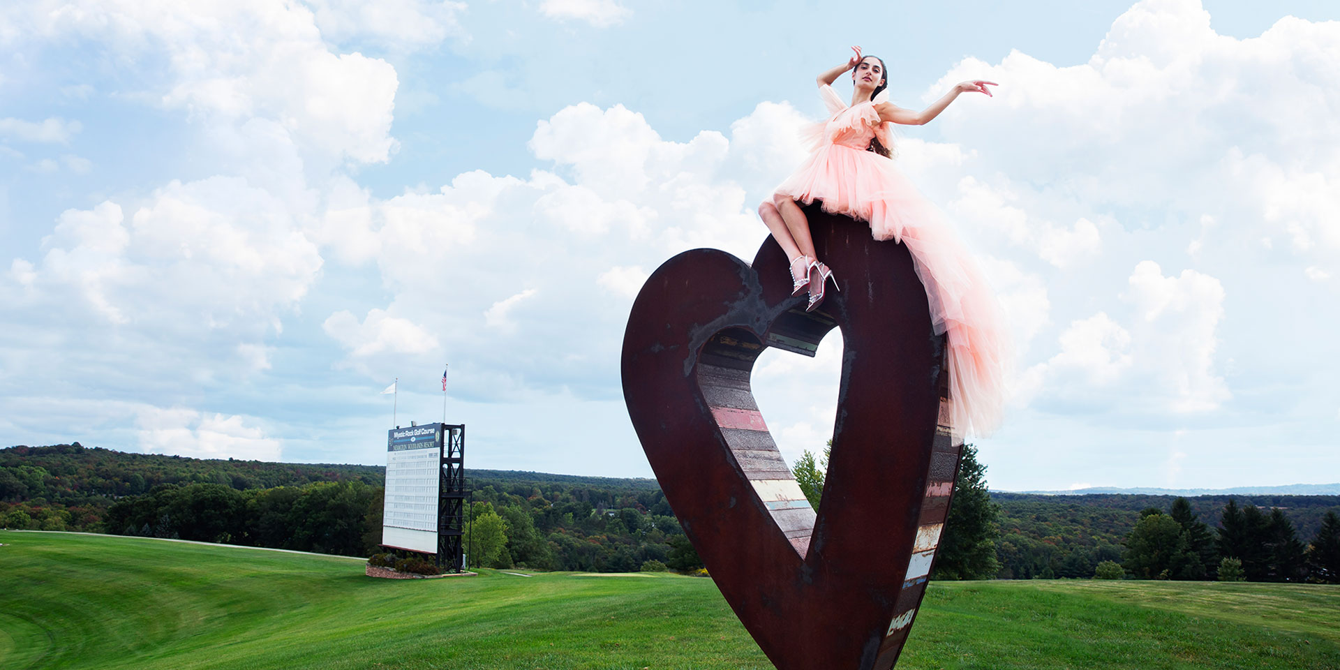 woman in a pink dress sitting on top of a heart sculpture outdoors