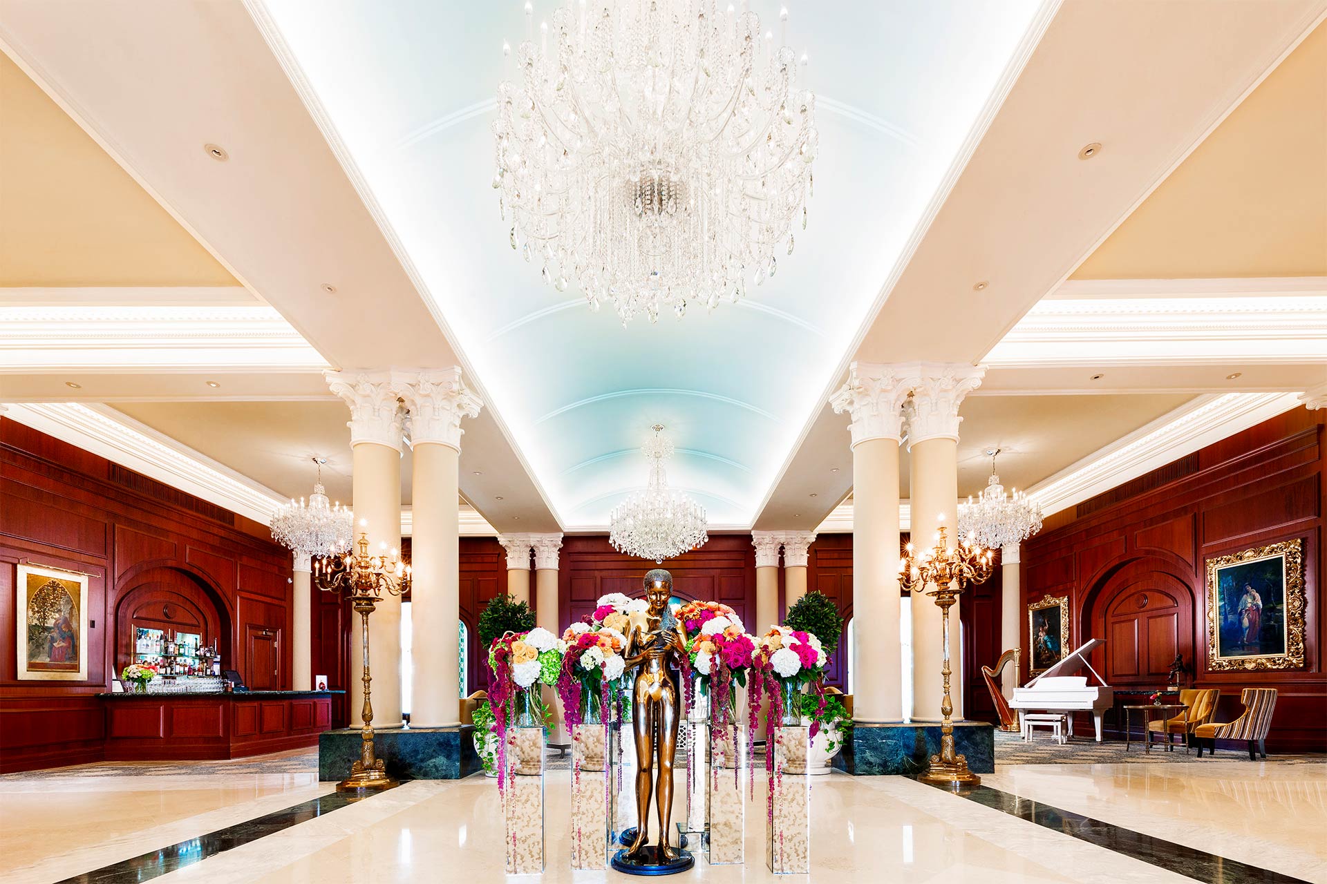 A fancy hotel lobby with a bronze statue of a woman in front and wooden walls and chandeliers above