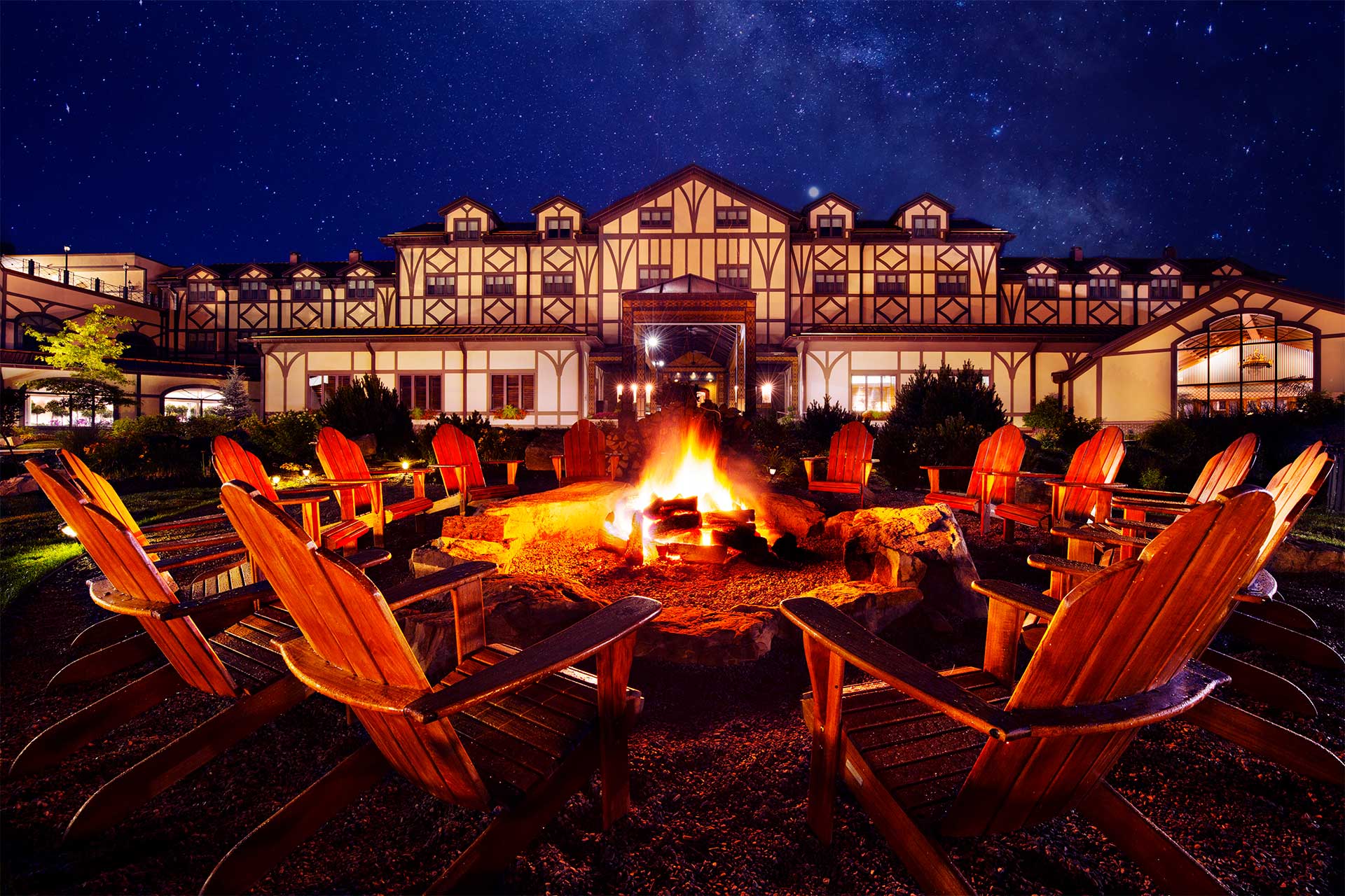 A large fire pit surrounded by chairs in front of a large lodge