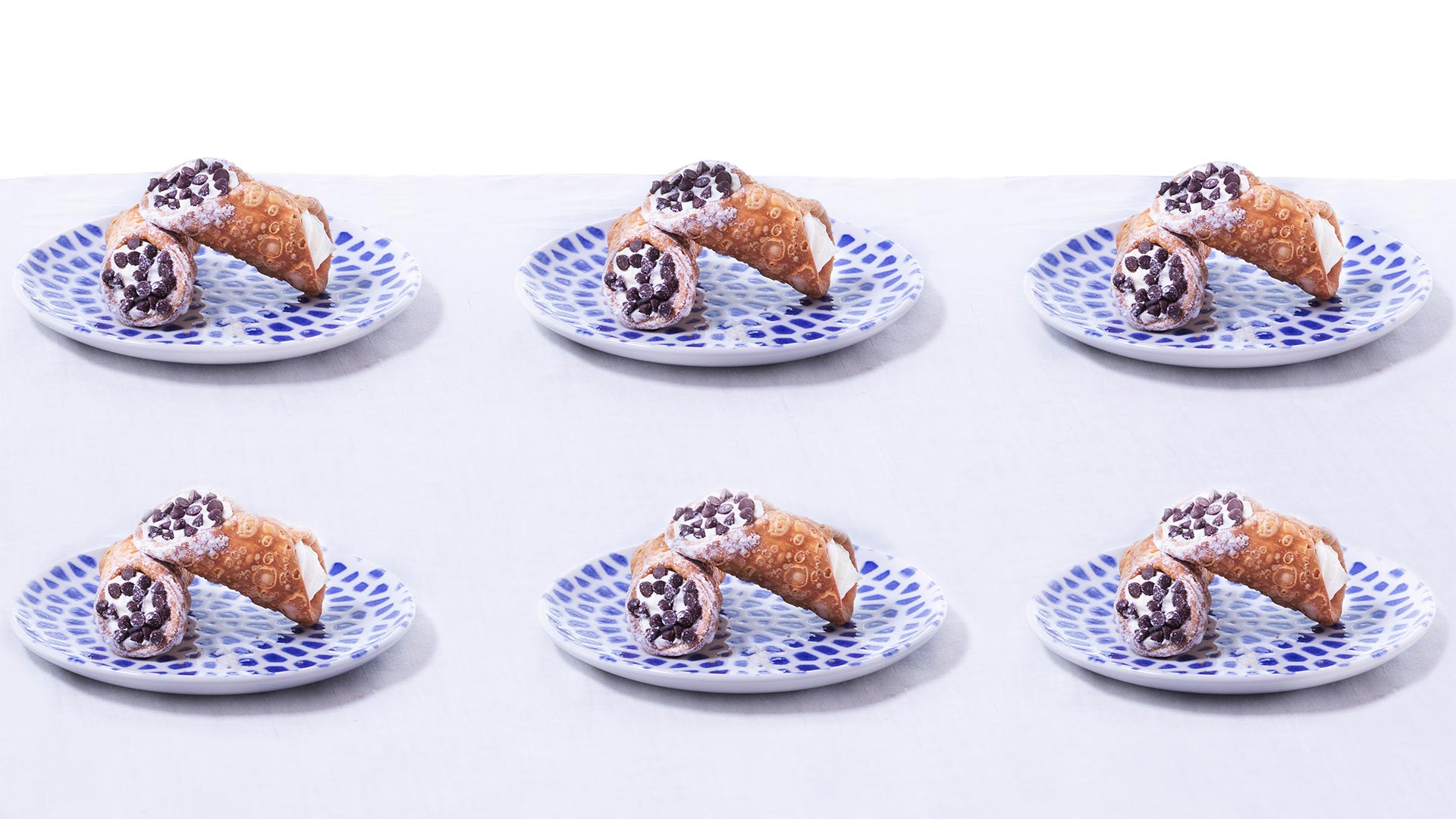 six cannolis on blue and white dotted plates