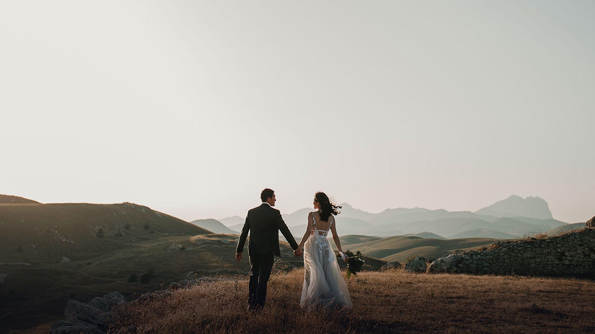 bride and groom holding hands and walking through a field with mountains