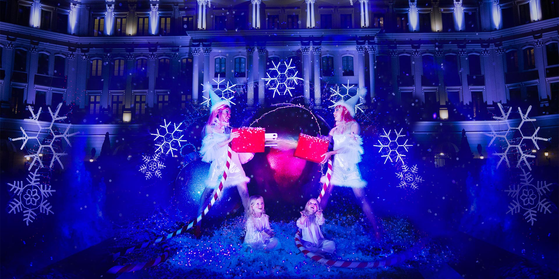 two elves holding up a giant plug in front of snowflake light show in front of hotel