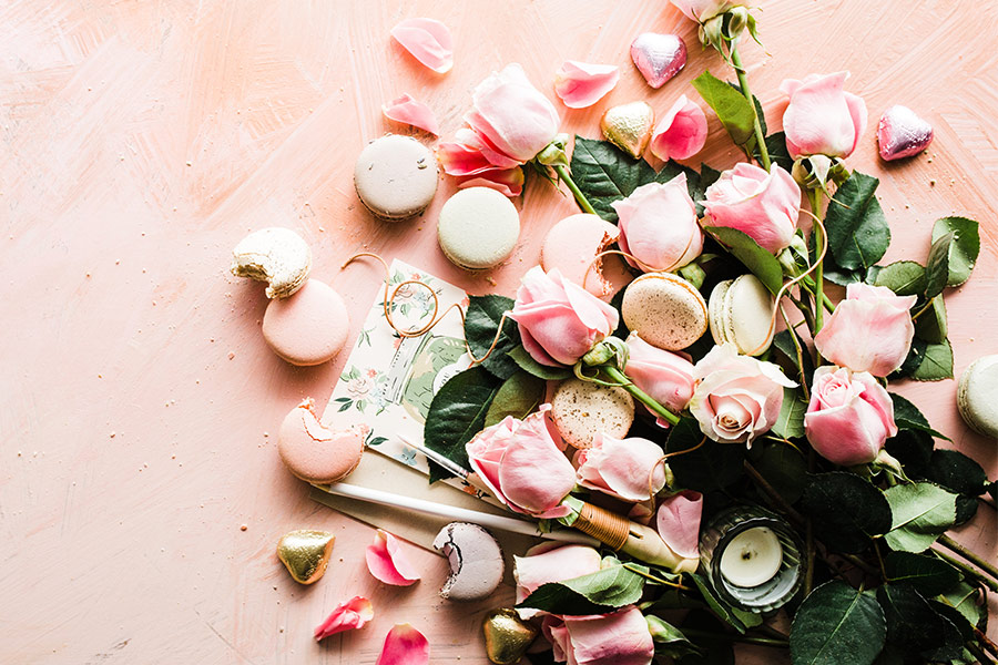 A beautiful array of pink roses with pink and white macarons scatter on a dusty baby pink background.