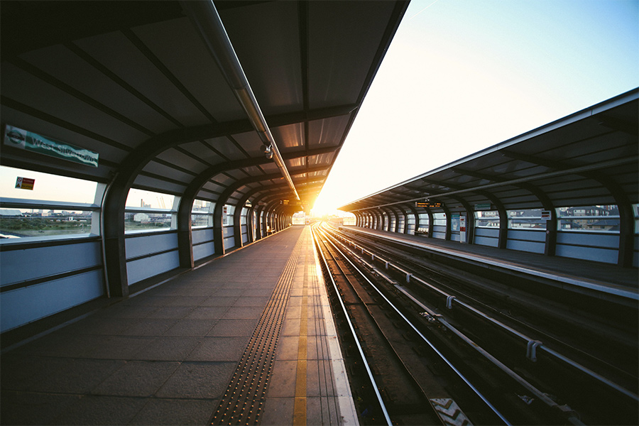 An empty train station platform with a beautiful sunset beaming from the middle.