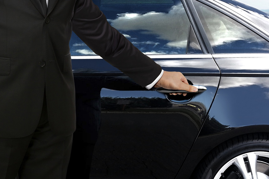 a chauffeur opening the door to a balck sleek car.