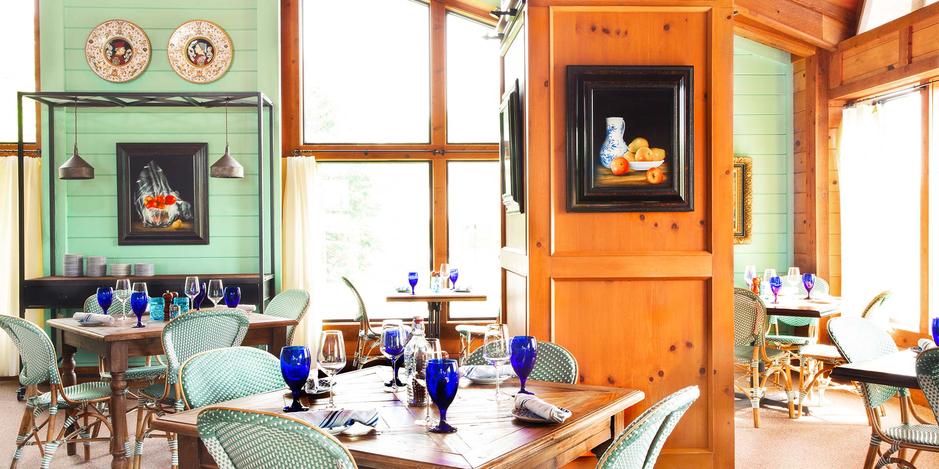 A dining table with blue glasses surrounded by teal chairs in a kitchen.