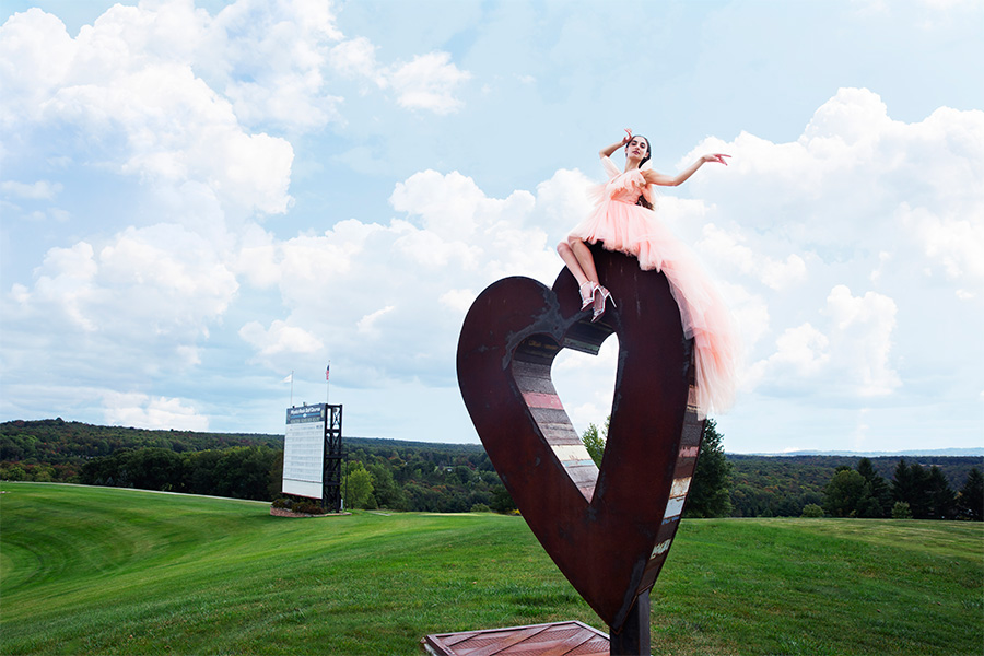 woman on a heart shaped sculpture in a green field