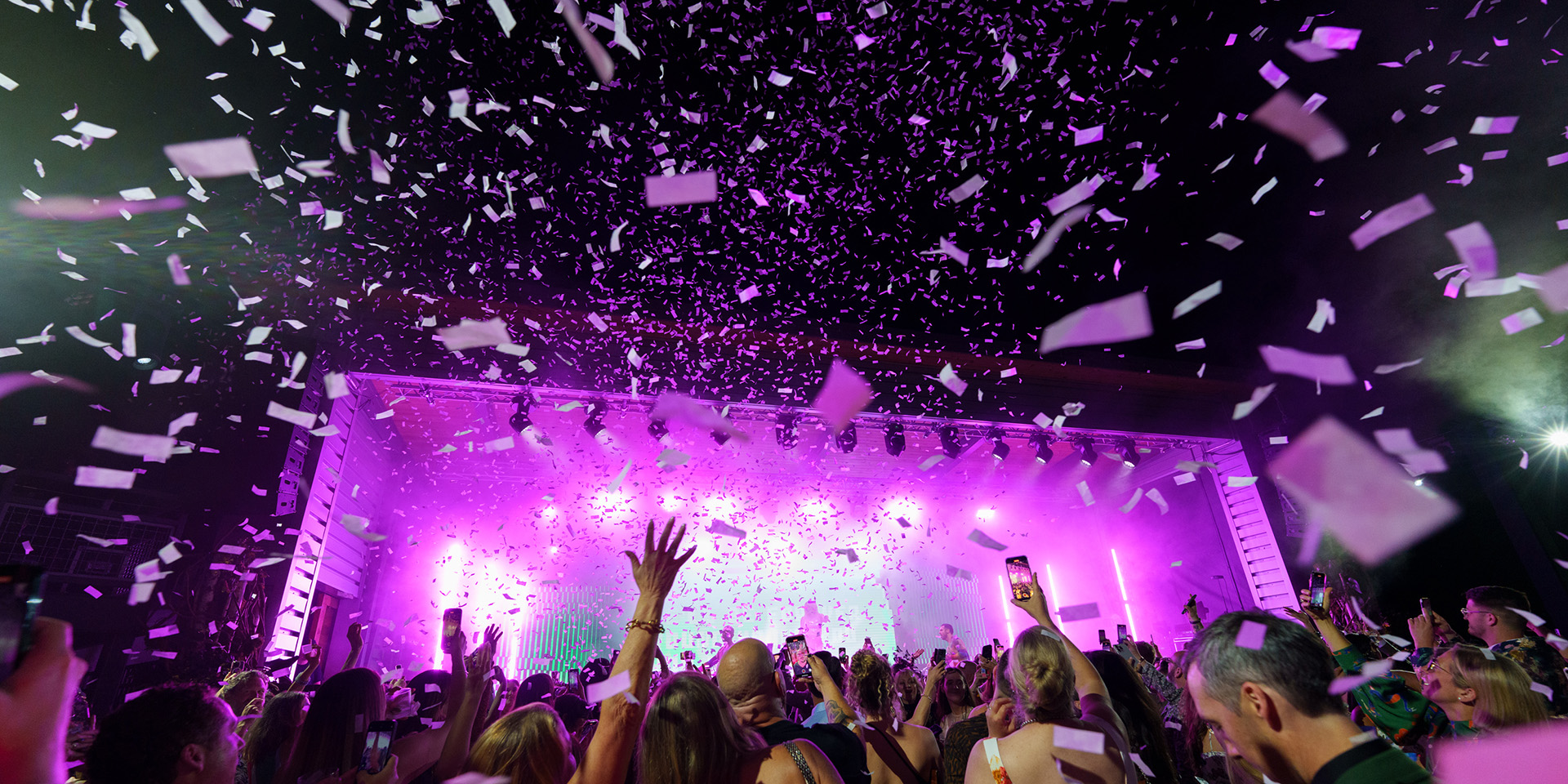 image of people at a concert with purple lighting and confetti falling