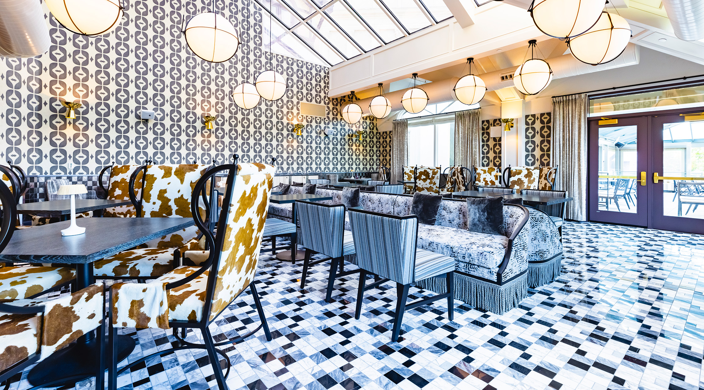 One of the numerous dining rooms inside Fawn & Fable in The Grand Lodge at Nemacolin, showing a tiles floor, unique and sumptuous furnishings, large skylights, and modern lighting