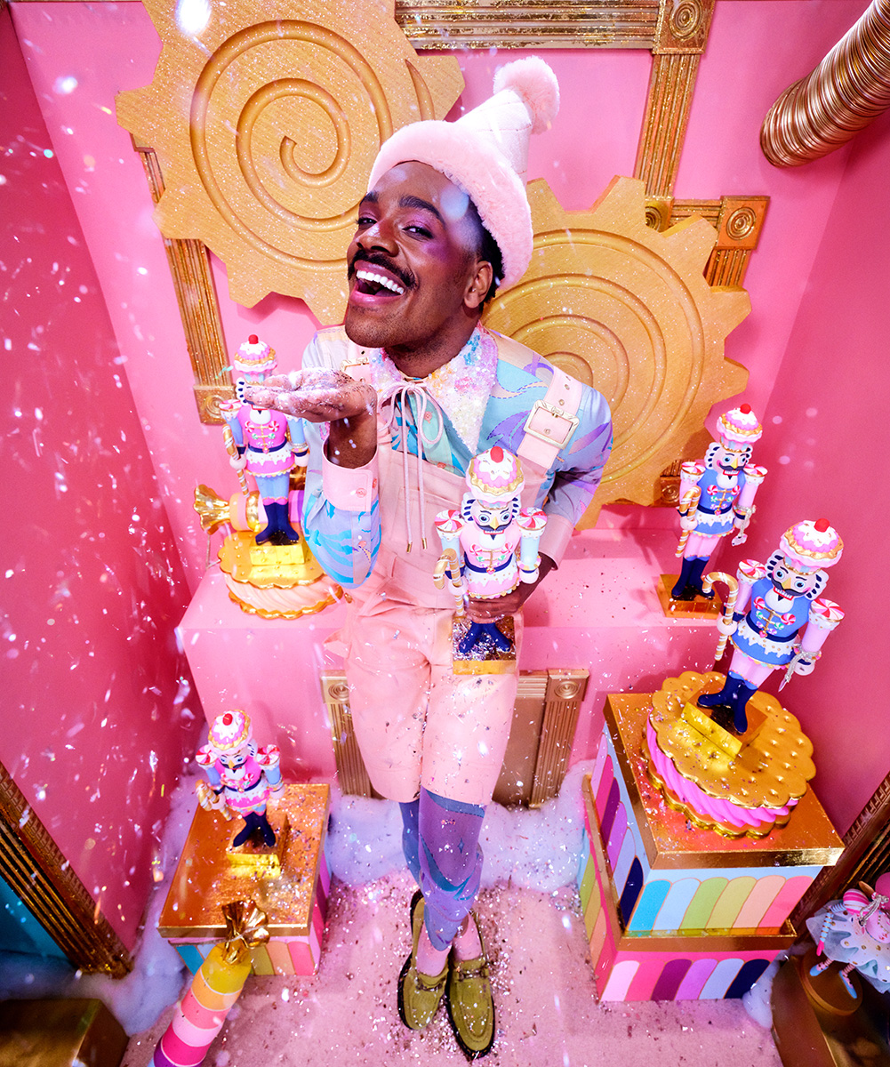 An adult elf in a pink outfit catches snow while surrounded by colorful presents and holiday nutcrackers at Nemacolin resort's Hardy's Holiday Village