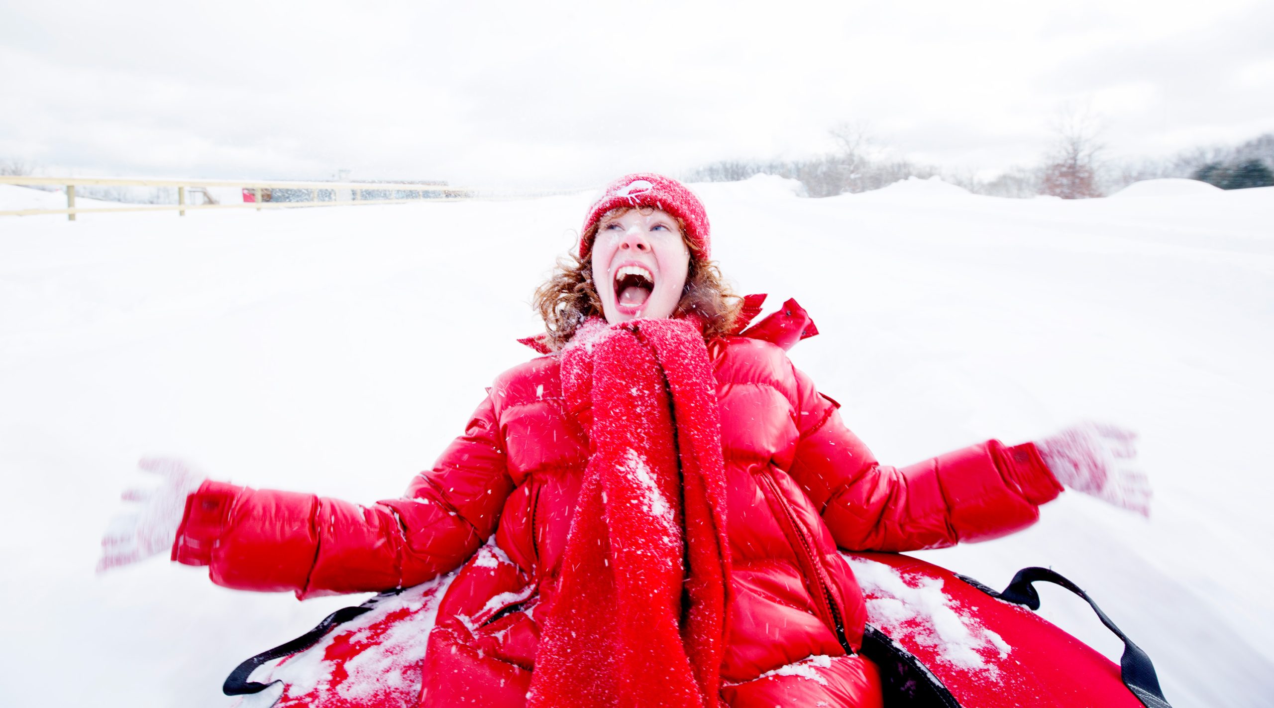 Red-haired woman in a red coat snow tubing down a hill at Nemacolin