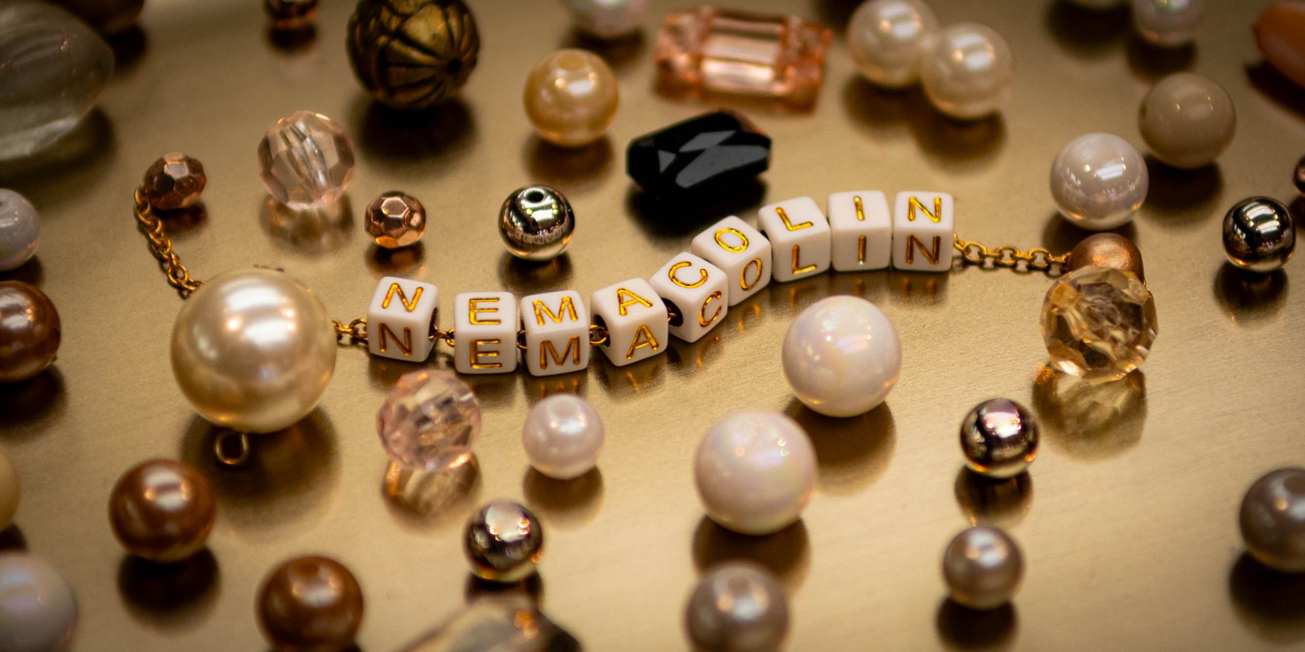 Assorted beads scattered on a tray around white, square beads that spell out the word "Nemacolin."