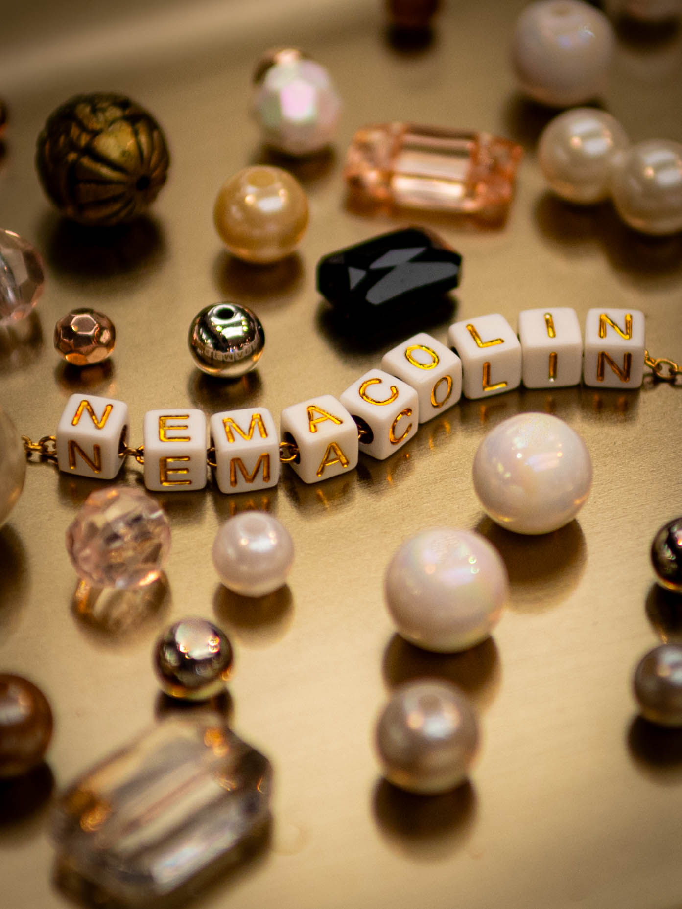 Assorted beads scattered on a tray around white, square beads that spell out the word "Nemacolin."