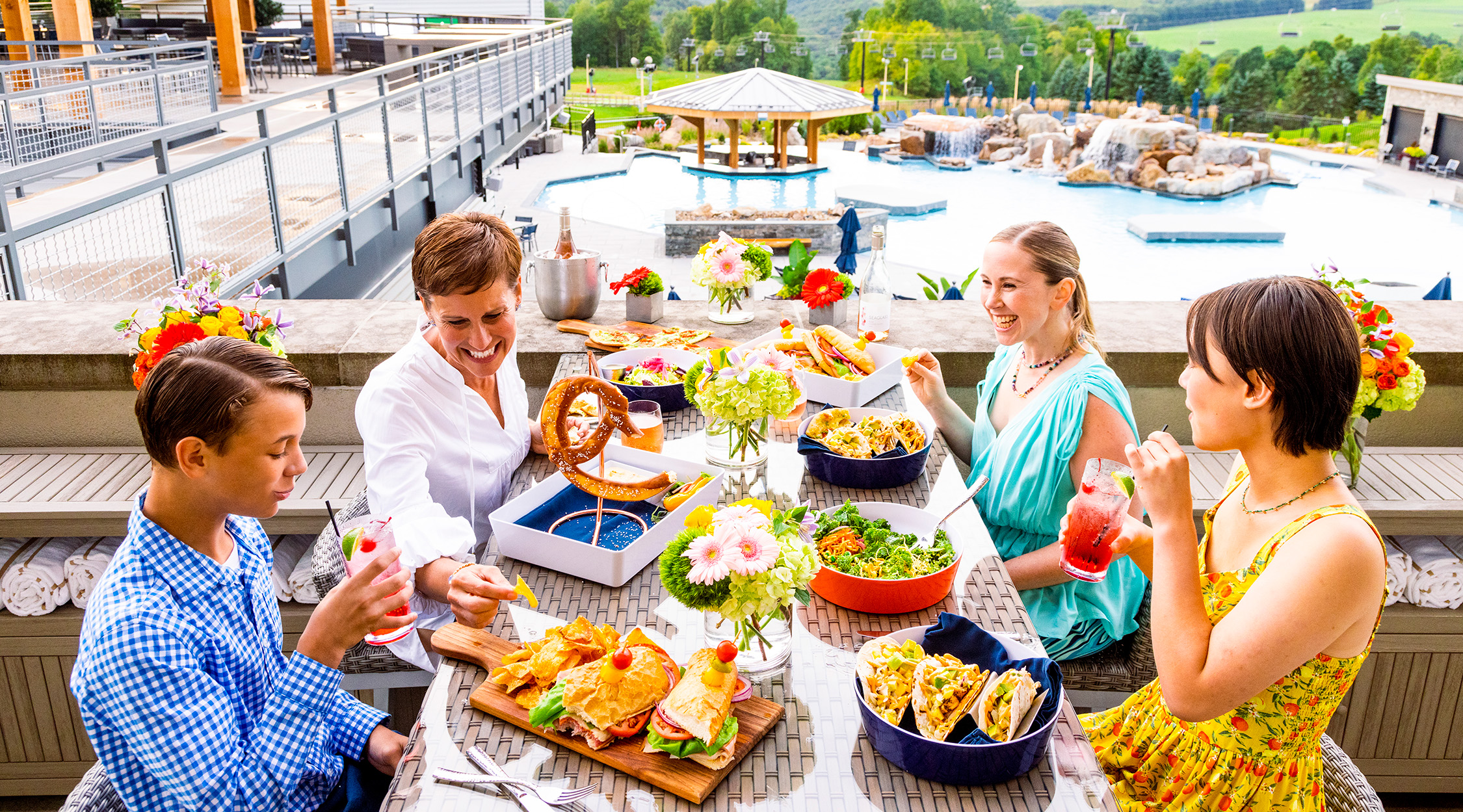 A family of four enjoying an outdoor meal overlooking the pool at The Peak restaurant at Nemacolin resort.