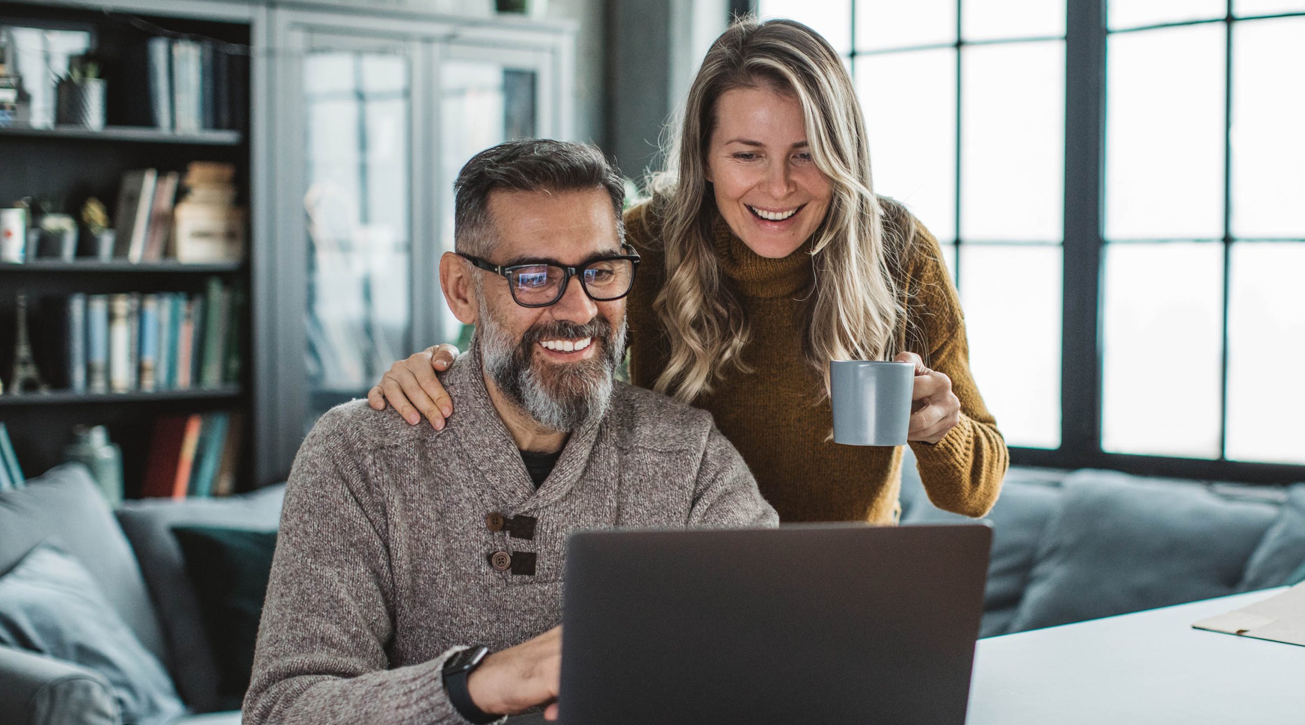 Mature couple smiling and at home using a laptop computer to view the screen together