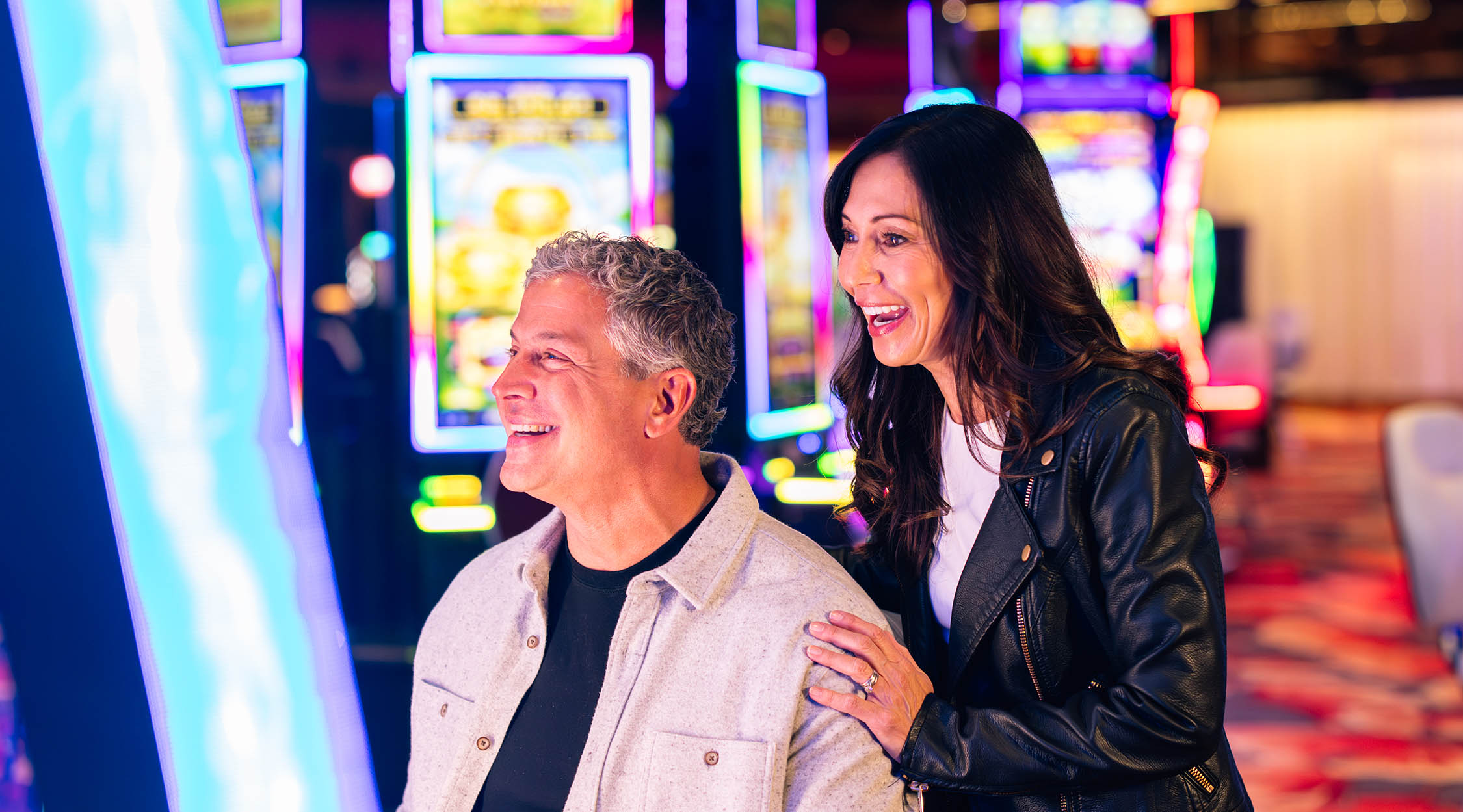 Two guests enjoying slot machines at Nemacolin's Casino, surrounded by colorful lights and gaming excitement.