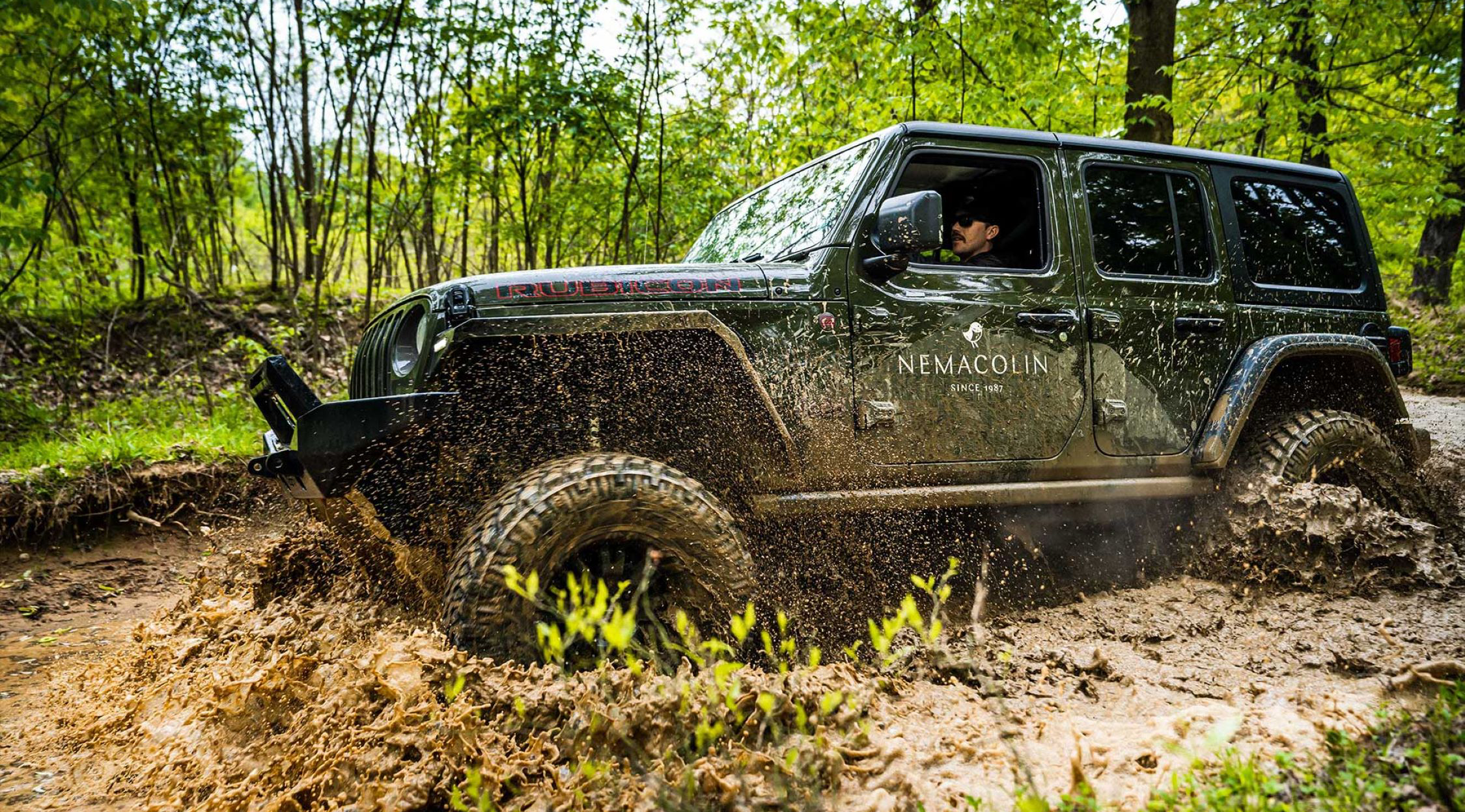 A green jeep with a Nemacolin resort logo off-roading through mud in a green forest