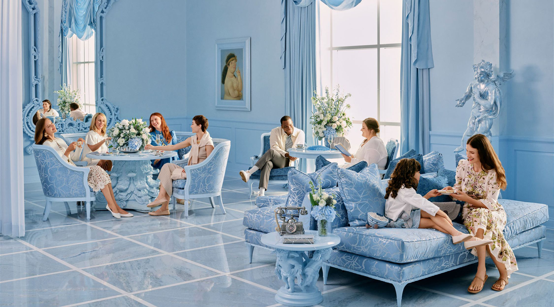 Several people sitting in three areas within a room with blue walls, blue flooring, and blue furniture having afternoon tea service in The Bleu Room at Nemacolin resort