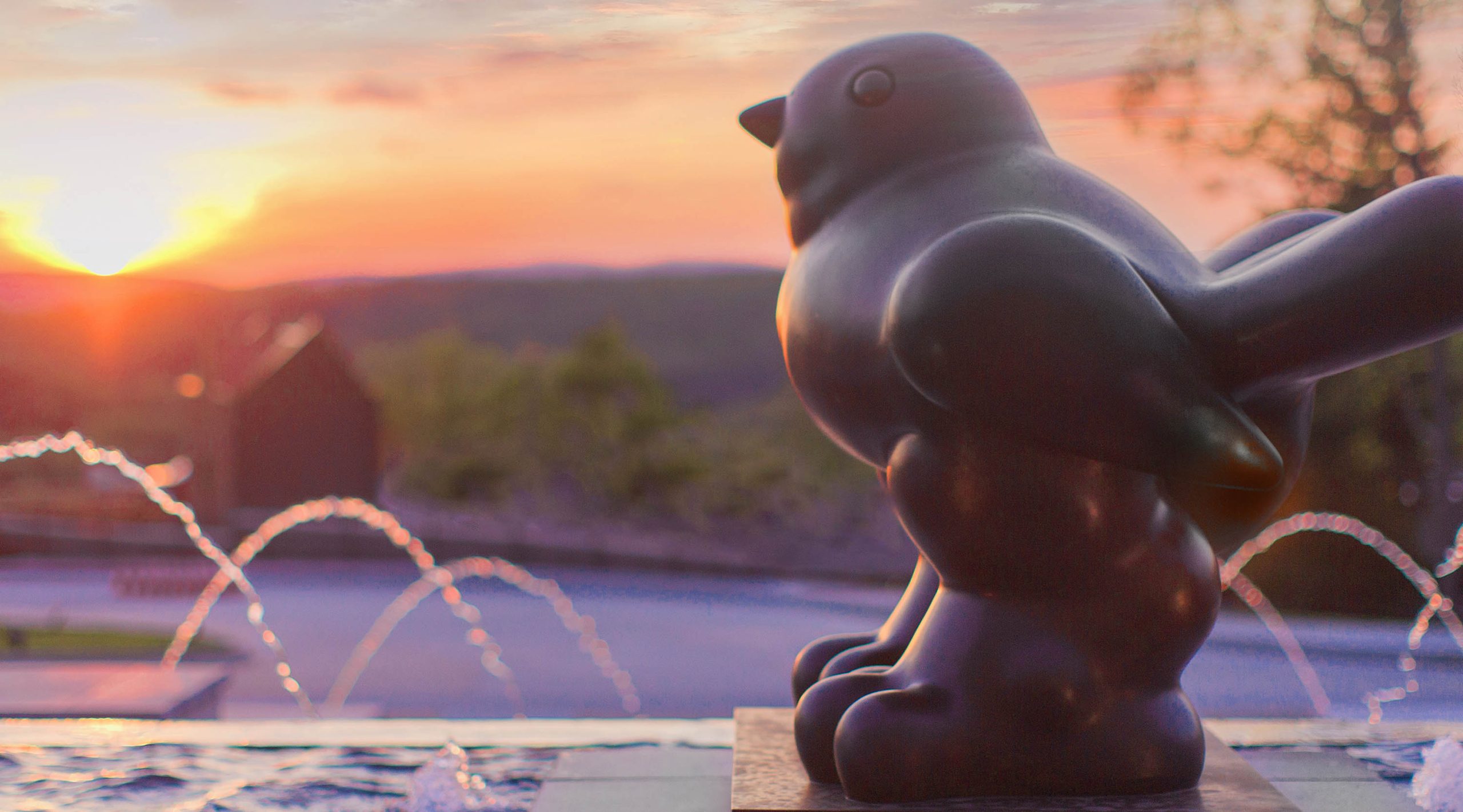 Botero's Little Bird sculpture from the Nemacolin art collection near a fountain at Nemacolin resort during a sunset