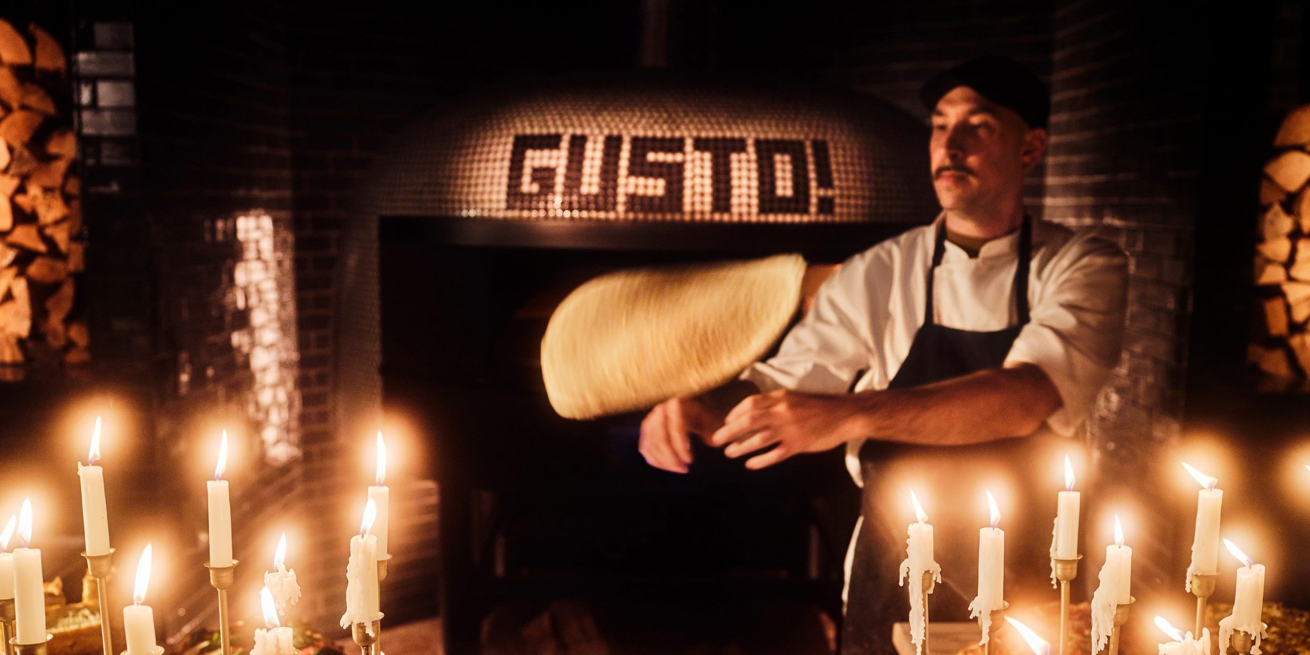 Person flipping pizza dough in front of an oven.