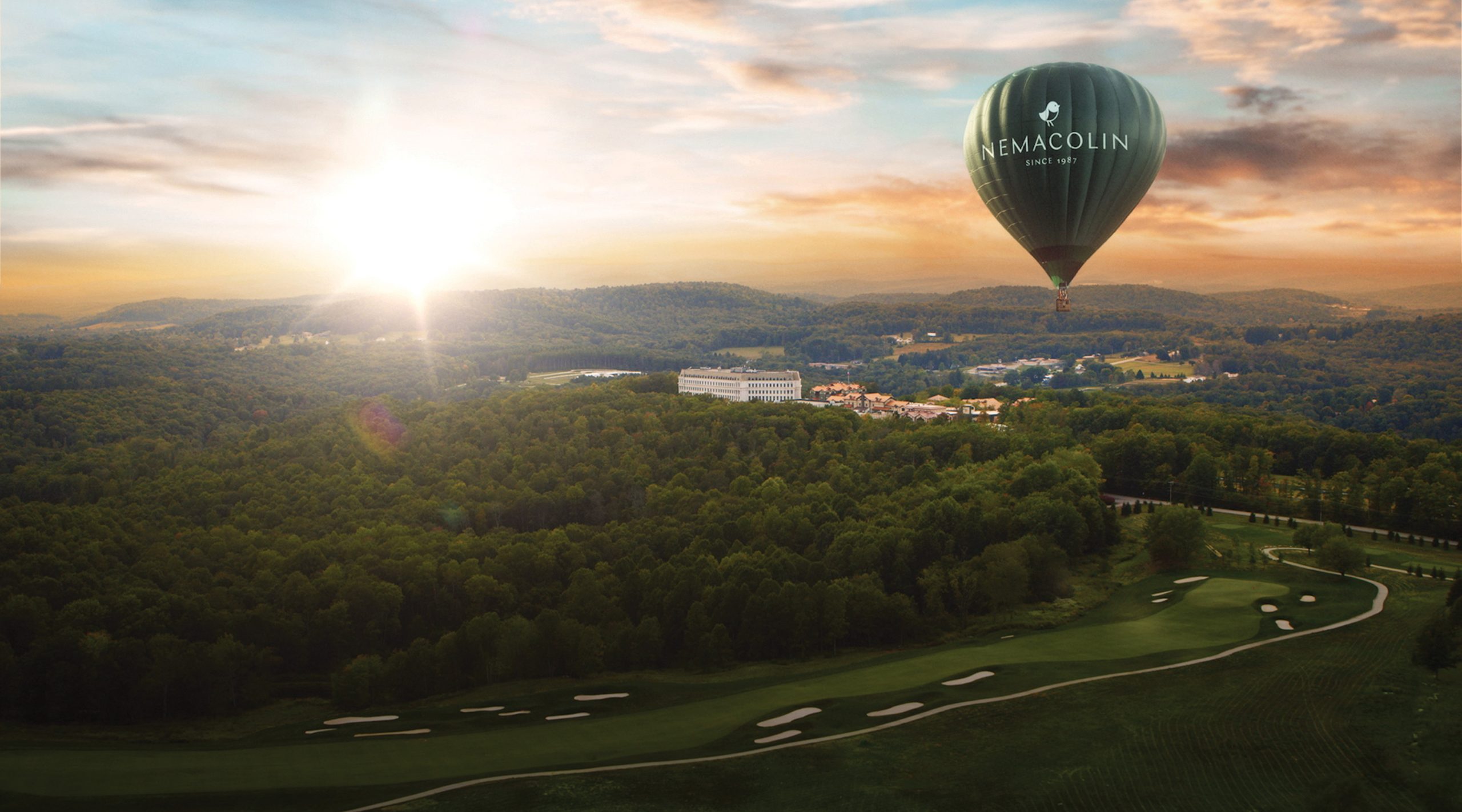 A hot air balloon in the sky at sunset, flying over a golf course and resort.