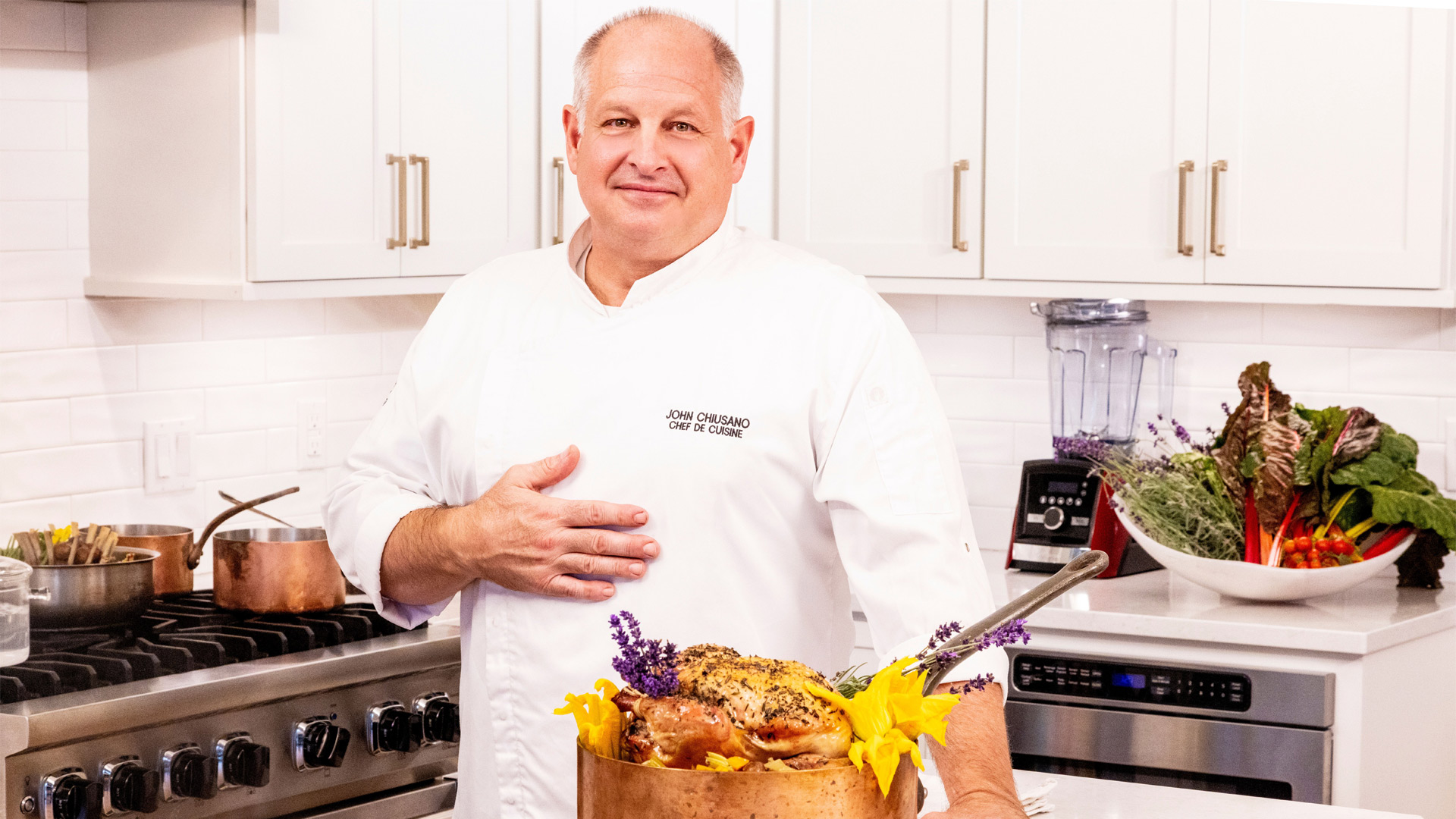 Chef John Chiusano, Chef de Cuisine at Nemacolin in Pennsylvania, presenting a farm-to-table roasted chicken with fresh herbs and edible flowers in the resort’s private dining kitchen.