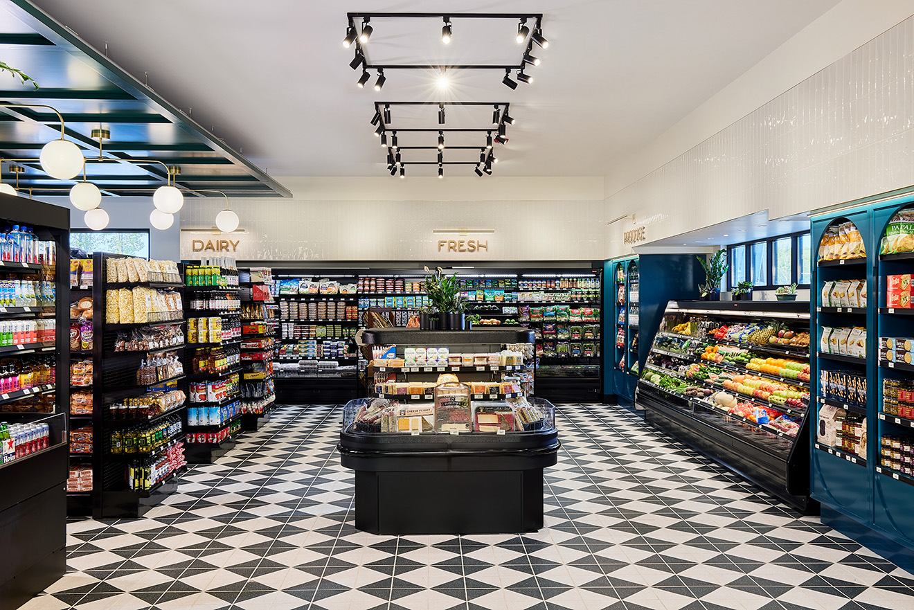 A modern grocery store interior with black and white checkered flooring, shelves stocked with various products, and a central island display with fresh produce. The lighting is bright, and the signage above the shelves indicates different sections like Dairy and Fresh.